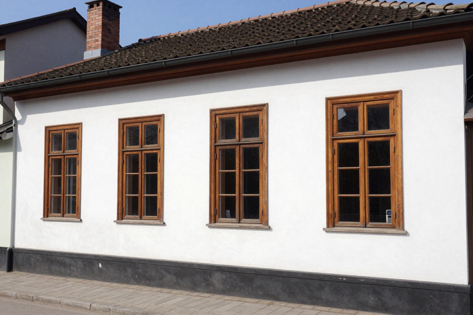 Fachada de la casona de un piso, estucada en blanco, con cuatro ventanas altas de madera y techo de teja