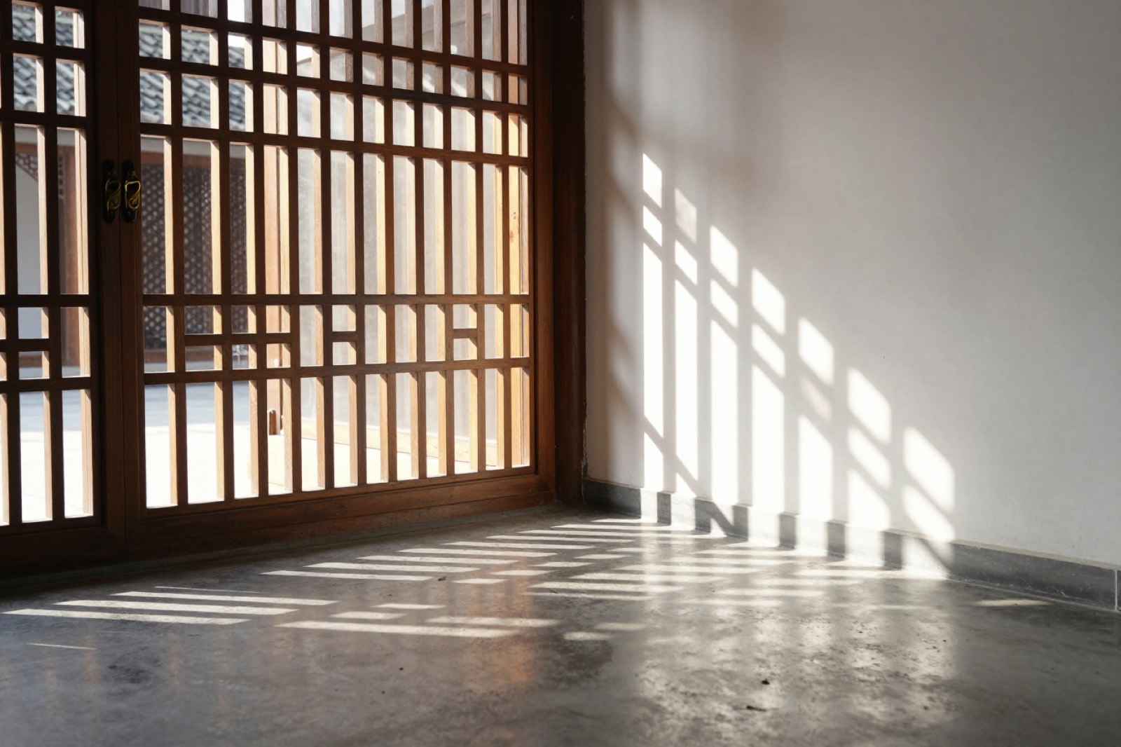Sol de tarde filtrado por una celosía de madera: franjas de luz sobre un muro blanco y un piso de hormigón