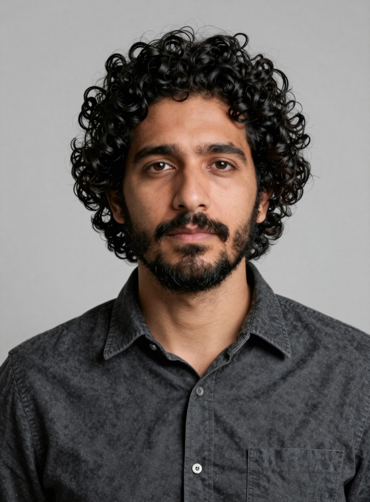 Retrato de Tomás Carvajal: hombre de pelo negro crespo y barba, camisa gris oscura